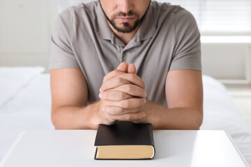 Wall Mural - Religious man with Bible praying at home, closeup