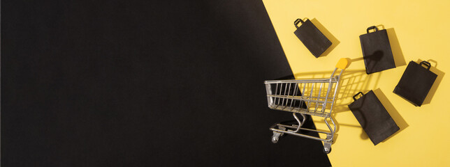 Wall Mural - Flat lay miniature supermarket cart with shopping bags in black friday sale on yellow background