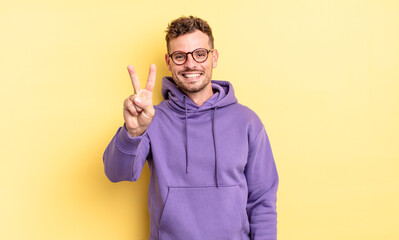 young handsome hispanic man smiling and looking friendly, showing number two or second with hand forward, counting down