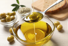 Pouring Fresh Olive Oil Into Spoon Above Bowl On Table, Closeup