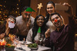 © Syda Productions - holidays, people and celebration concept - multiethnic group of happy friends with party props having christmas dinner at home and taking selfie with smartphone