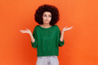 © khosrork - Confused woman with Afro hairstyle wearing green casual style sweater spreading hands aside, dont know what to do, looking away. Indoor studio shot isolated on orange background.