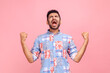 © khosrork - Portrait of overjoyed handsome man with beard in casual shirt expressing winning gesture with raised fists and screaming, celebrating victory. Indoor studio shot isolated on pink background.