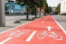 Traffic, City Transport And People Concept - Woman Cycling Along Red Bike Lane With Signs Of Bicycles And Two Way Arrows On Street