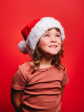 Cheerful Cute Kid In Santa Hat Smiling In Red Studio