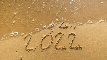 Wall Mural - message year 2021 replaced by 2022 written on beach sand background. good bye 2021 hello to 2022 lap