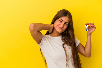 Wall Mural - Young caucasian woman holding a home keys isolated on yellow background touching back of head, thinking and making a choice.