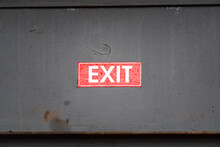 "Exit" Red Sticker Sign Which Is Sticked On Grey Rusty Metal Wall. Emergency Sign Object Phot. Selective Focus.