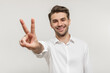 © Anastasia - Young happy man with beard wearing white shirt standing over white background smiling and showing two fingers on camera hand doing victory sign. Number two.