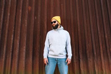 Wall Mural - City portrait of handsome hipster guy with beard wearing gray blank hoodie with space for your logo or design. Mockup for print. Hoodie template