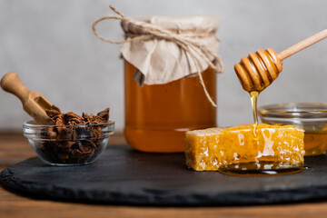 Wall Mural - honeycomb, wooden dipper, bowl with anise seeds and blurred jar with fresh honey on slate board and grey background