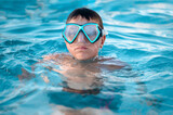 Fototapeta Przestrzenne - A child, a teenager in a swimming mask swims in clear blue water in a pool, pond or ocean, close-up.