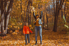 Single Parent Family Playing With Autumn Leaves In Park. Happy Mom And Son Throw Autumn Leaves Up In Fall Park.