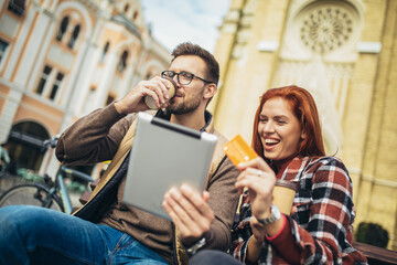 Wall Mural - Trendy young couple in town using tablet and credit card.