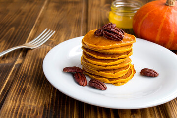 Wall Mural - Close-up on homemade pumpkin pancakes with honey and pecans in the white plate on the rustic background