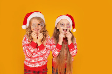 Wall Mural - little beautiful happy blonde girls in a New Year's jumper in plaid trousers and Santa Claus hats are holding the numbers 2022 on a yellow background