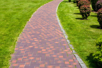 Wall Mural - curved stone tile pavement crescent, path in park landscaped with green grass and bushes, garden landscape on a sunny summer day.