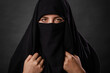 Close up portrait of young, adult woman in black burqa  with hidden face, isolated on black background.