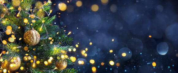 Wall Mural - christmas tree in blue night - golden balls on fir branches with defocused lights in abstract backgr