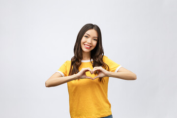 Wall Mural - Portrait of a smiling young asian woman showing heart gesture with two hands and looking at camera isolated over white background.