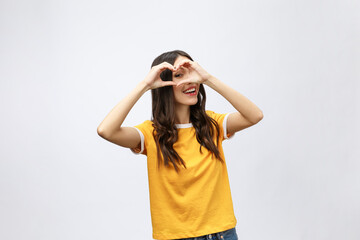 Wall Mural - Portrait of a smiling young asian woman showing heart gesture with two hands and looking at camera isolated over white background.