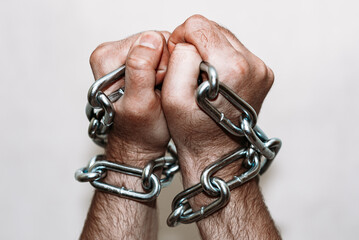 Men's hand in a steel chain.Steel chains in the hands of man on a gray wall background.Toned.Closeup,selective focus.