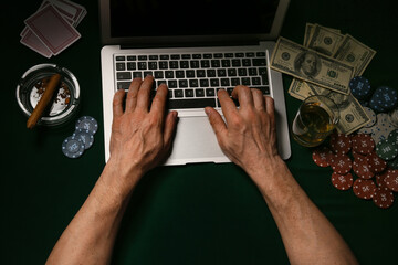 Man with laptop playing poker online at table in casino