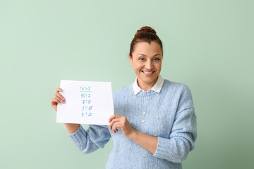 Portrait of female teacher with mathematical tasks on paper sheet against color background