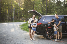 Portrait Of Mother, Father And Two Daughters Standing By Car At Electric Vehicle Charging Station