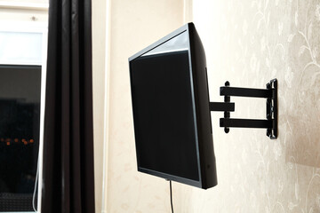 Swivel TV bracket LED display. Side view. X-shaped red fasteners. Black color. Multiplanar. Hangs on a wall. Reliable and comfortable fastening. Childproof and rollover protection. Metallic equipment