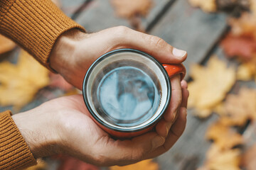 Autumn drink tea or coffee in hands on the background of October yellow leaves. Autumn comfort and mood background concept.