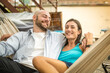 © MandriaPix - young couple lying on hammock, people relaxing on vacation, happy lovers hugging and having a rest on a terrace on sunset, warm filter