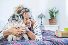 Happy Woman Embracing Pug On Bed At Home