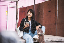 Smiling Female Teenager With Mobile Phone Sitting On Boardwalk