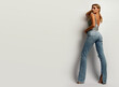 Young tanned woman in jeans and shiny top in the studio on a white background.Model posing in the studio.Advertising fashion clothes.Advertising concept.