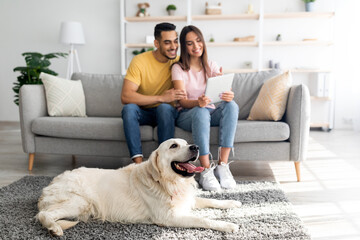 Poster - Affectionate diverse couple using tablet on couch, cute pet dog lying on the floor at home, selective focus