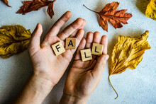 Hands Holding Wooden Blocks Spelling The Word Fall Surrounded By Autumn Leaves