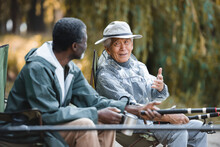 Senior Asian Man Talking To African American Friend While Fishing Outdoors