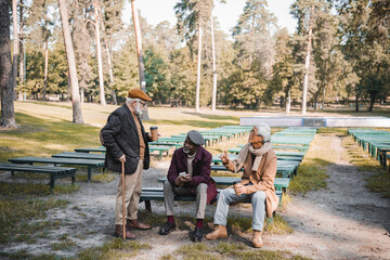 Wall Mural - Multiethnic men with smartphone and coffee to go talking in autumn park