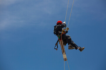 Male workers control swing rope down height tank rope access inspection of thickness tank gas background blue sky.