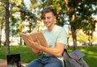 © Prostock-studio - Education concept. Teenage student guy reading book outdoors and preparing for exams, sitting in campus