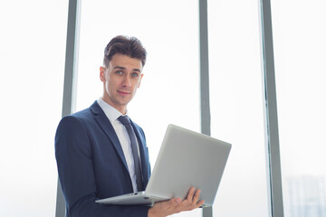 Portrait of adult smart business man in suit outfit standing and using laptop in modern workplace