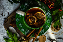 Cup Of Spiced Mulled Tea On A Table With Holly, Spices, String, Gift Tag And Scissors