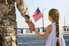 Soldier And His Little Daughter With American Flag Holding Hands Outdoors, Back View. Veterans Day In USA