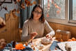 © Caterina Trimarchi - Cozy pumpkins. Woman making colorful fabric pumpkins. Autumn decoration with handmade textile pumpkin on wooden table. Fall vibes. Thanksgiving decor.