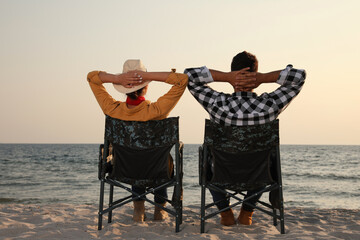 Poster - Couple sitting in camping chairs and enjoying seascape on beach, back view