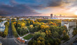 Park in Riga with trees in autumn colors. Colorful sunset over the city panorama. Downtown in background.