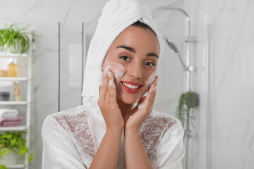 Poster - Beautiful young woman applying cleansing foam onto face in bathroom. Skin care cosmetic