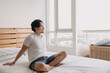 © Sevendeman - Happy Asian man sits and relax on his bed in his apartment.