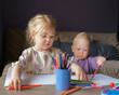 © Nata Bene - Adorable little girl with golden hair and cute baby boy drawing with colored pencils while sitting at table, older sister playing with small brother while enjoying leisure time together at home